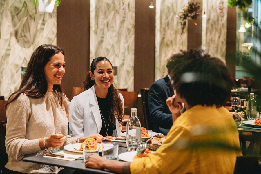 Group of four colleagues enjoying a meal together at a restaurant, talking, smiling, and having a good time