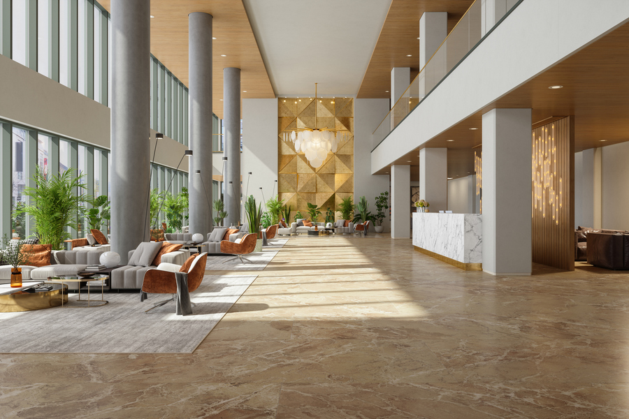 Spacious and luxurious hotel lobby featuring marble floors, tall windows with abundant natural light, modern lounge seating, indoor plants, and a contemporary reception desk.